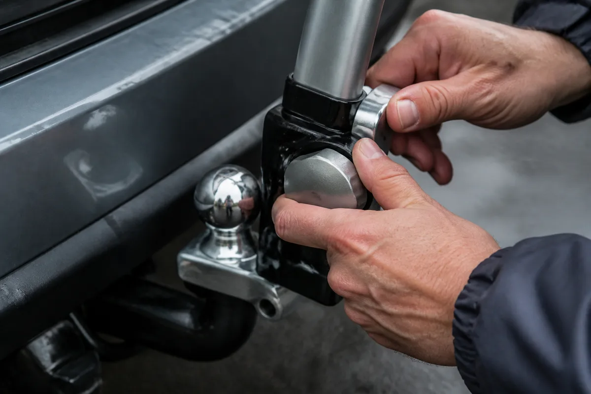 Mains serrant la molette de fixation d’un porte-vélos sur la boule d’attelage d’une voiture